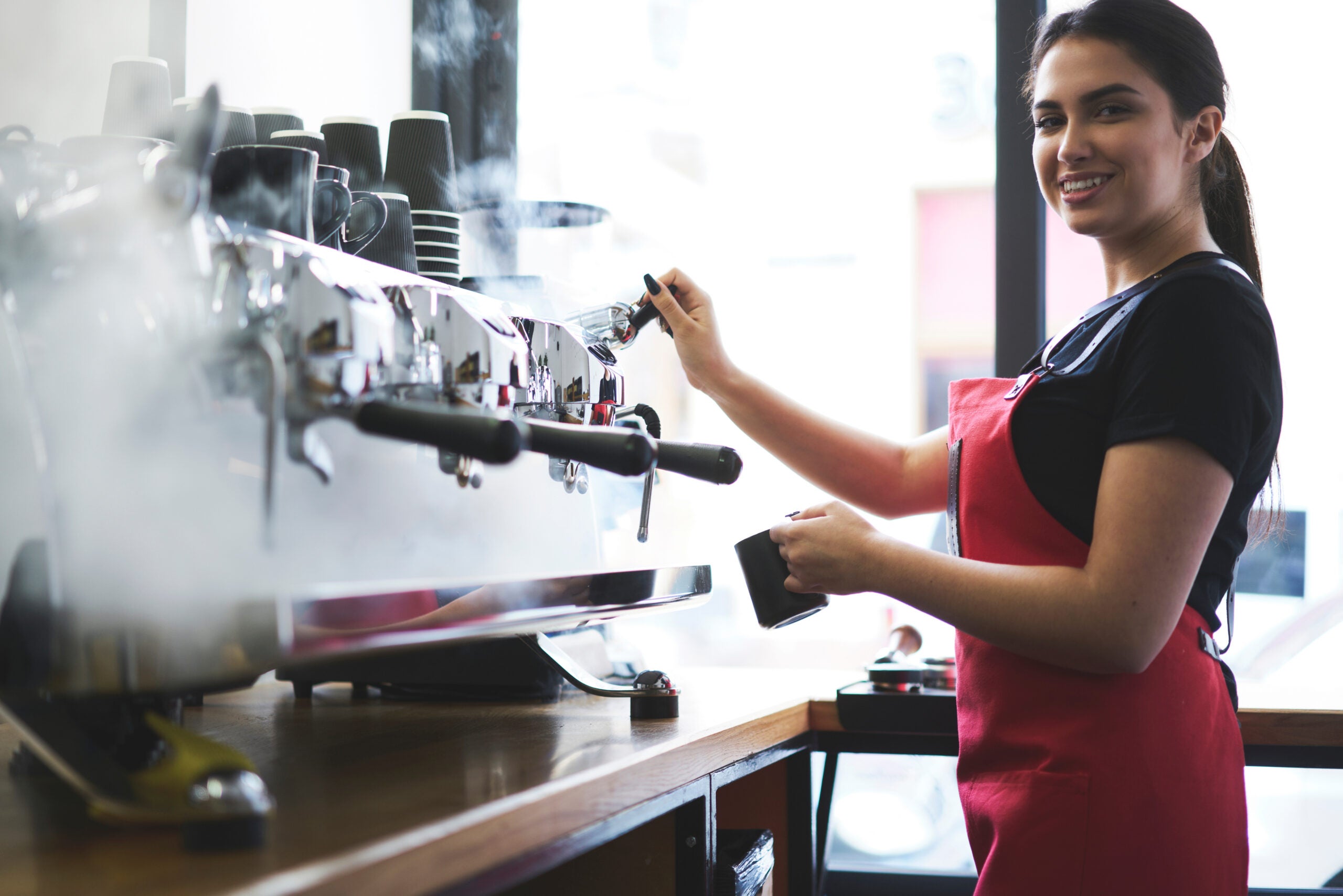 Smiling young trainee in uniform learning how to temperate drinks with steam