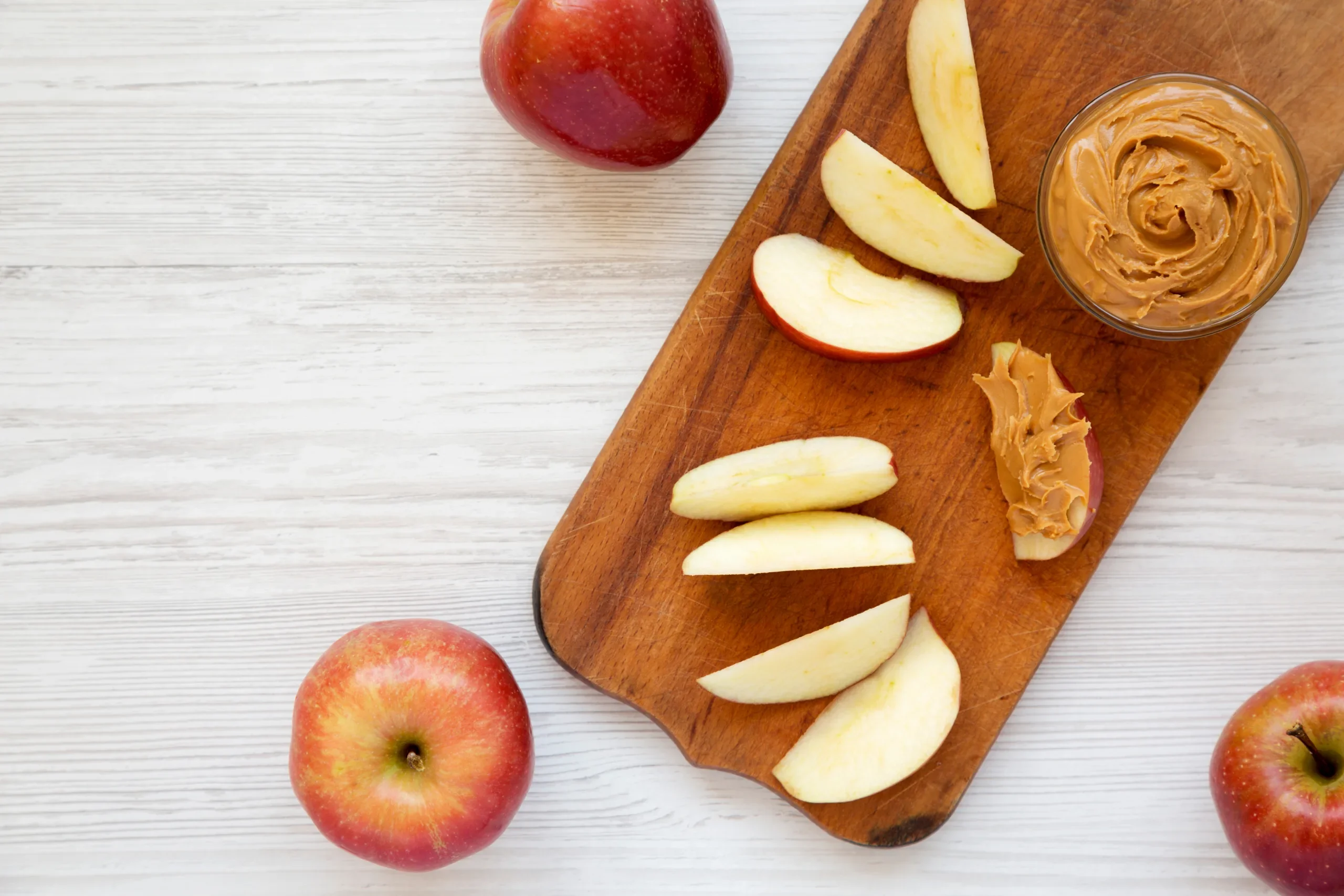 Raw Red Apples and nut Butter on a rustic wooden board on a white wooden table, top view.