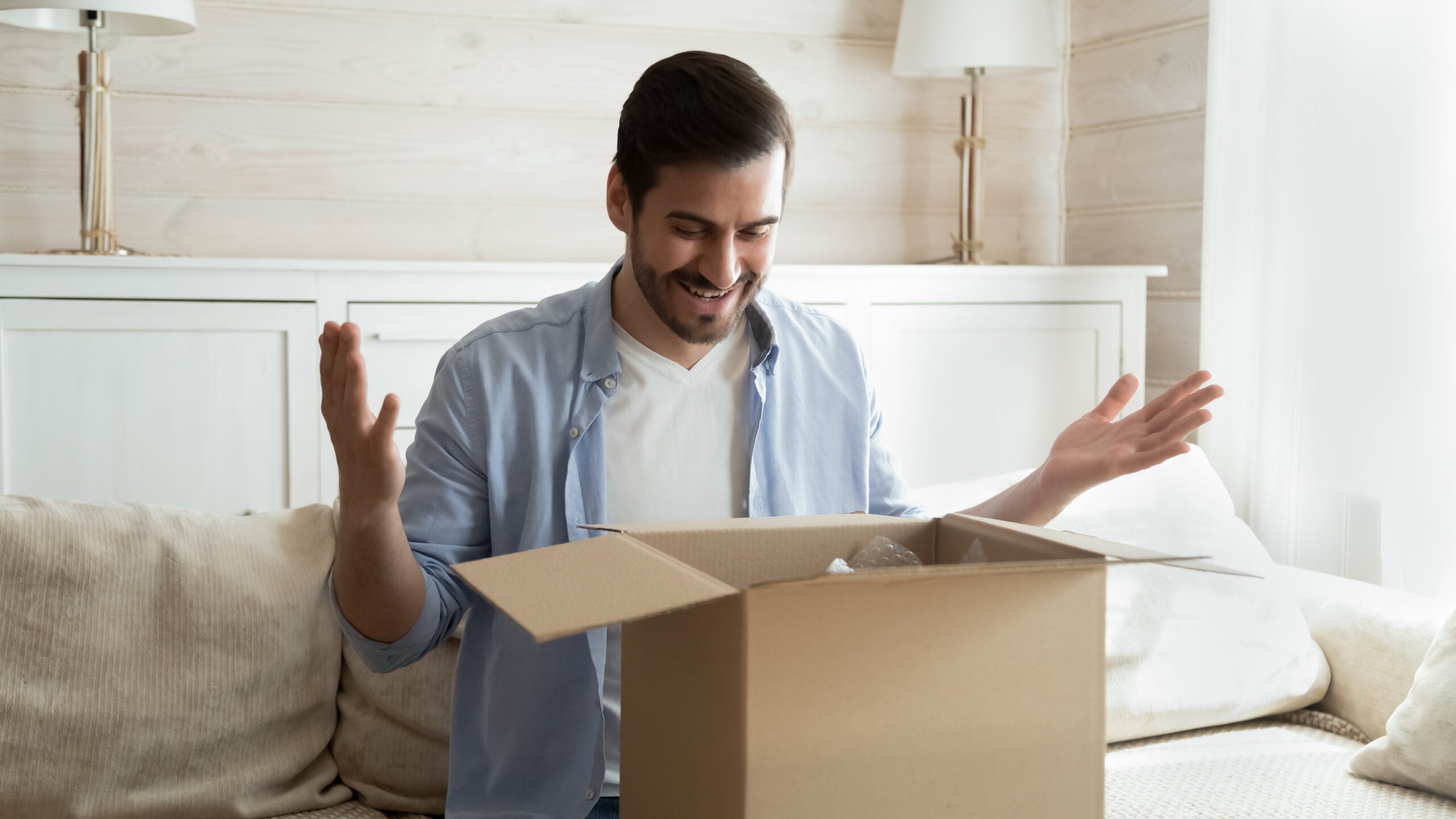 Just what I wanted. Glad happy young man sit on couch opening box with gift surprise send by beloved person, millennial vlogger recording promotional video of unpacking parcel with sponsor products