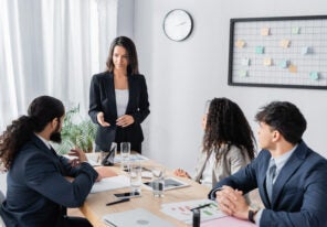 businesswoman standing and pointing with hand at co-worker during business meeting in office