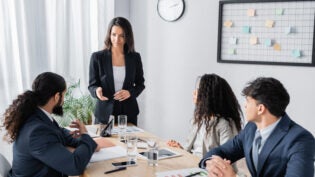 businesswoman standing and pointing with hand at co-worker during business meeting in office