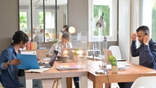 View of co-workers in open space office protected by plexiglas