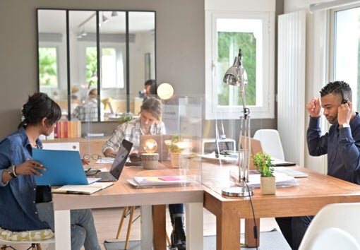 View of co-workers in open space office protected by plexiglas