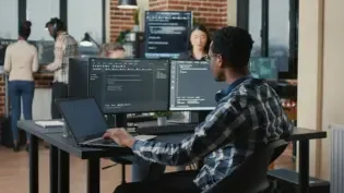 Portrait of programer fixing glasses while typing on laptop smiling satisfied about compiling results sitting at desk