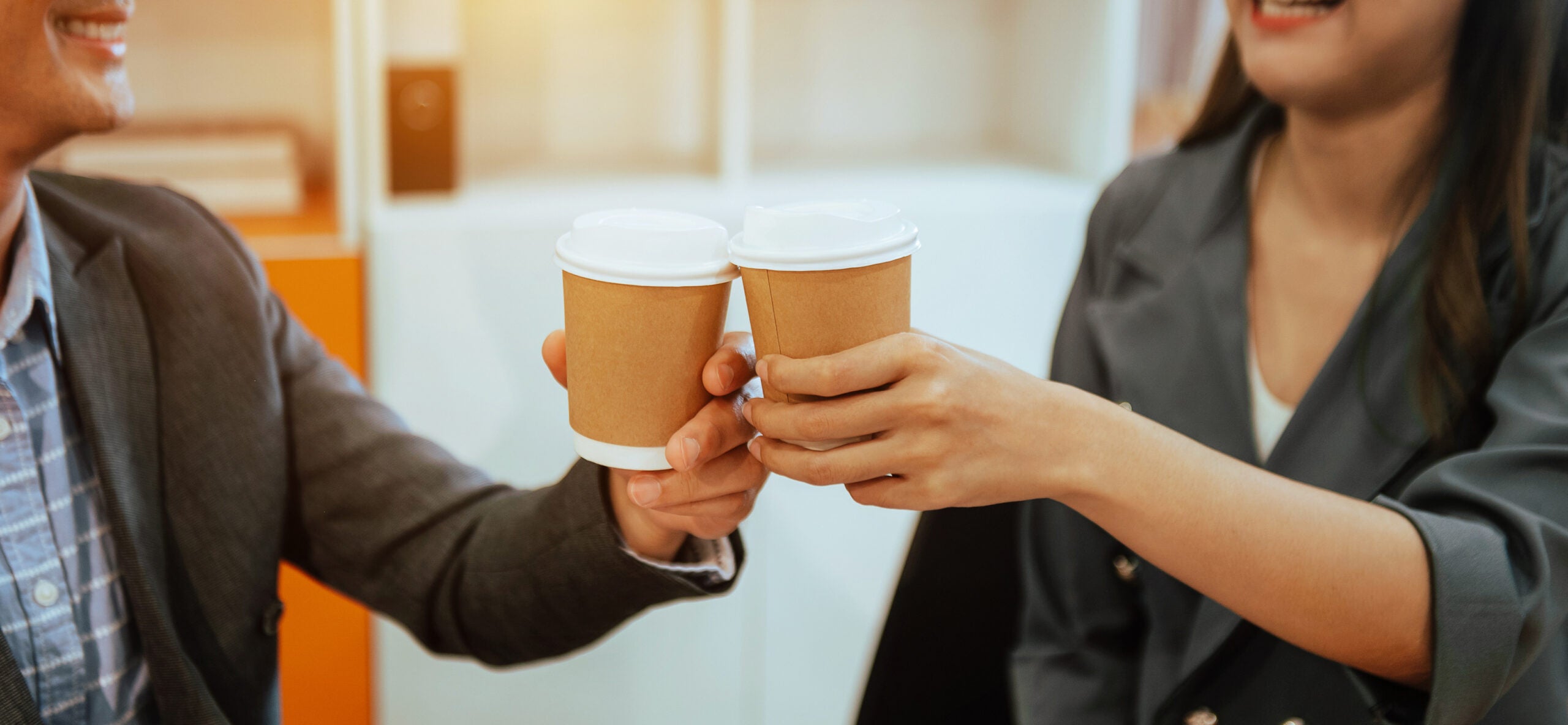 Two business people standing and holding a coffee cup in modern office