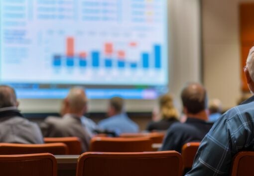 A senior citizen sits in a lecture hall listening to a speaker present a financial planning seminar
