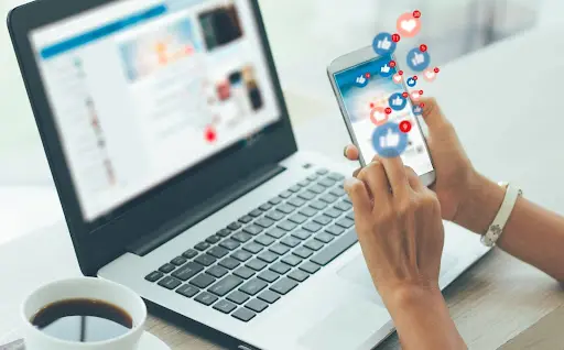 hands holding mobile phone in front of laptop