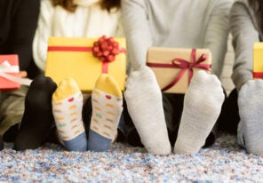 close up group of diverse friends feet with socks holding gift boxes and sitting on carpet mat in living room