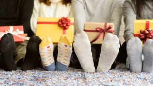 close up group of diverse friends feet with socks holding gift boxes and sitting on carpet mat in living room