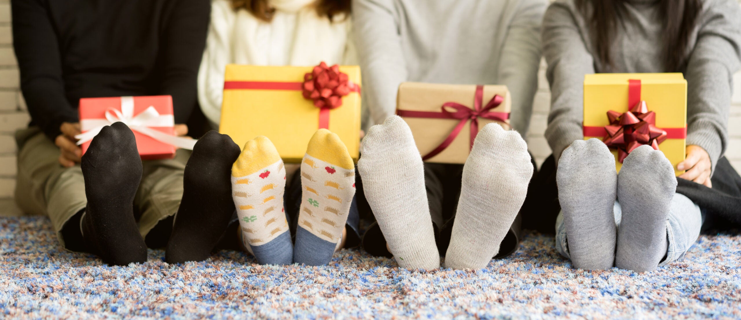 close up group of diverse friends feet with socks holding gift boxes and sitting on carpet mat in living room