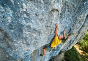 top view of man rock climber in yellow t-shirt, climbing on a cliff