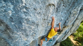 top view of man rock climber in yellow t-shirt, climbing on a cliff