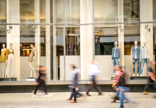 Motion blurred people walking past retail shop window on London