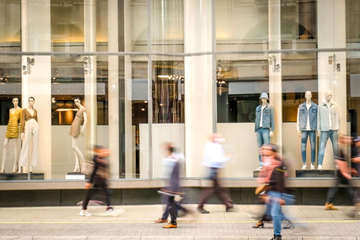 Motion blurred people walking past retail shop window on London