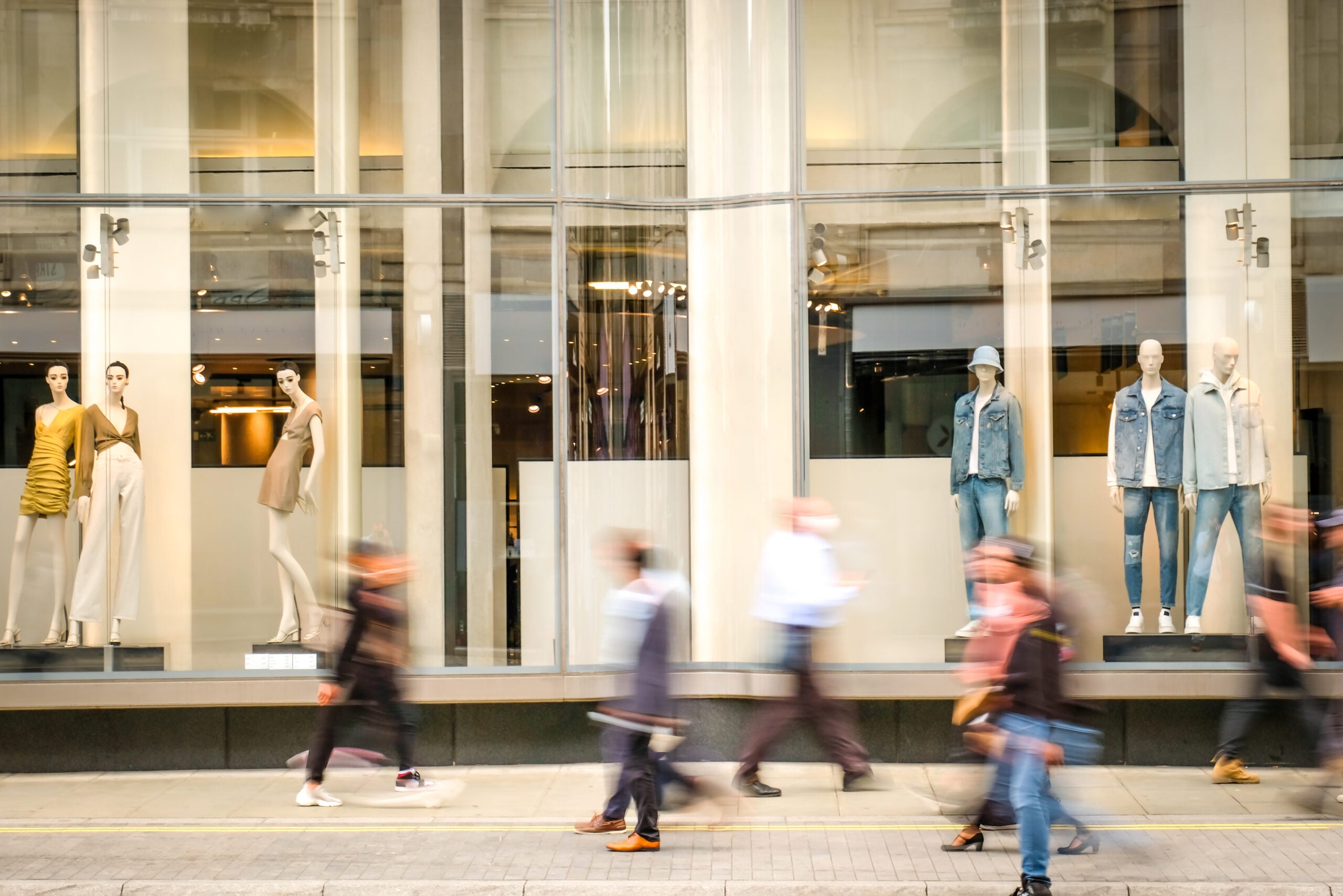 Motion blurred people walking past retail shop window on London