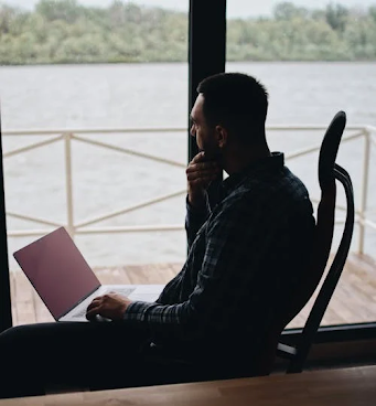 Man staring thoughtfully over water with laptop