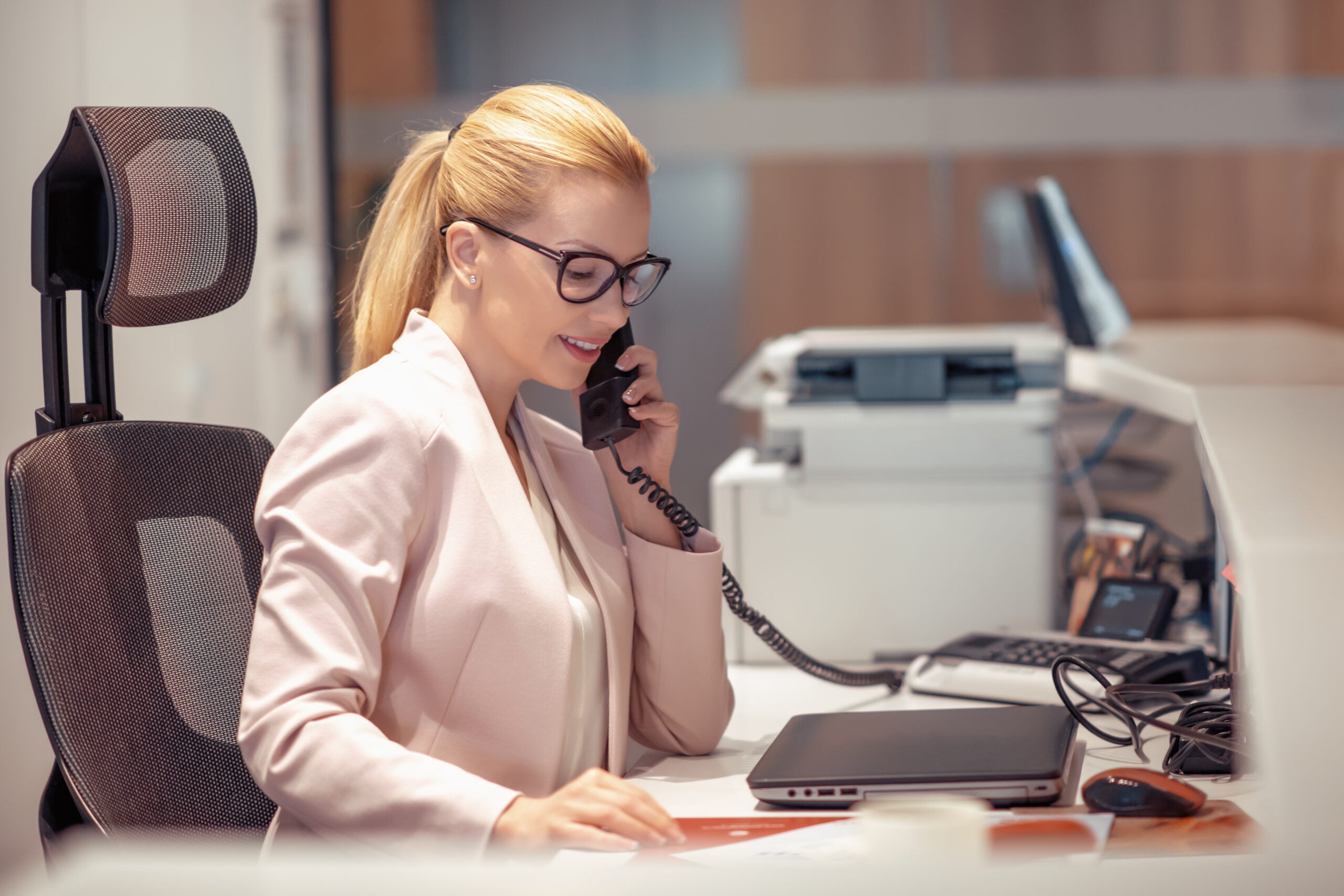 Young female receptionist talking on phone in office