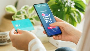 woman paying an order online with the phone and a credit card from home.