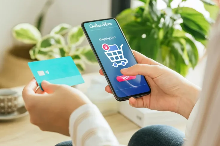 woman paying an order online with the phone and a credit card from home.