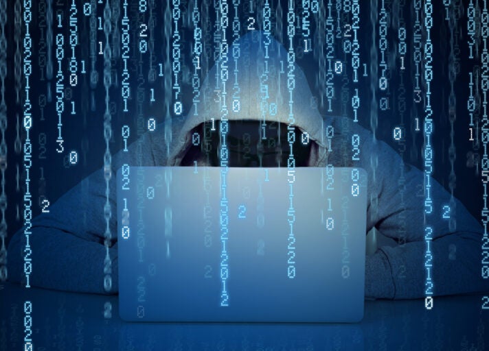 Young faceless man hacker working on a laptop on a binary code background