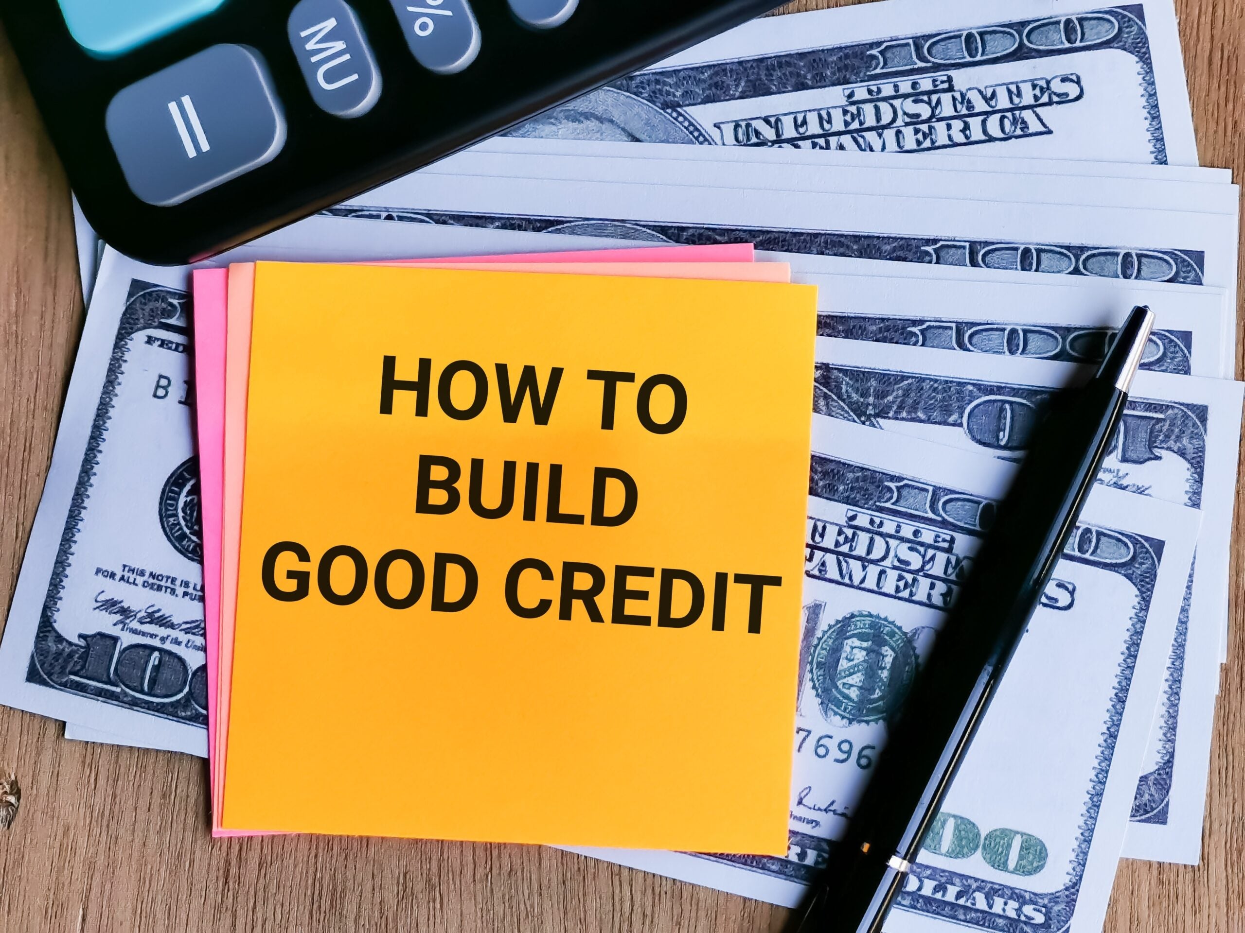 Phrase HOW TO BUILD GOOD CREDIT written on sticky note with calculator,fake money and a pen.