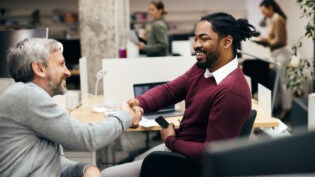 Happy male entrepreneurs shaking hands while greeting at corporate office.