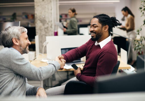 Happy male entrepreneurs shaking hands while greeting at corporate office.