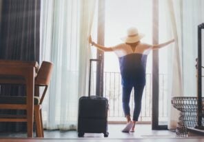 Woman staying in a hotel room with luggage.Open the curtain and door in the room looking to outside view.