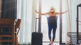 Woman staying in a hotel room with luggage.Open the curtain and door in the room looking to outside view.