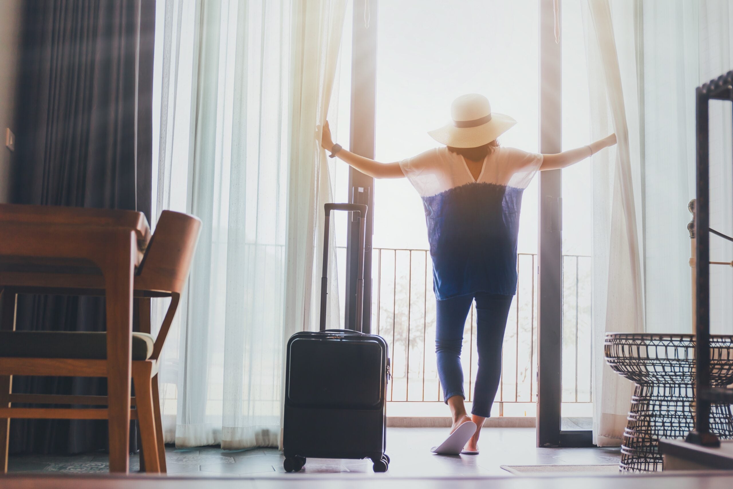 Woman staying in a hotel room with luggage.Open the curtain and door in the room looking to outside view.