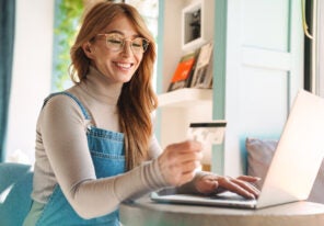 Photo of smiling woman holding credit card while using on laptop