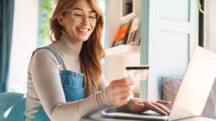 Photo of smiling woman holding credit card while using on laptop