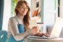 Photo of smiling woman holding credit card while using on laptop