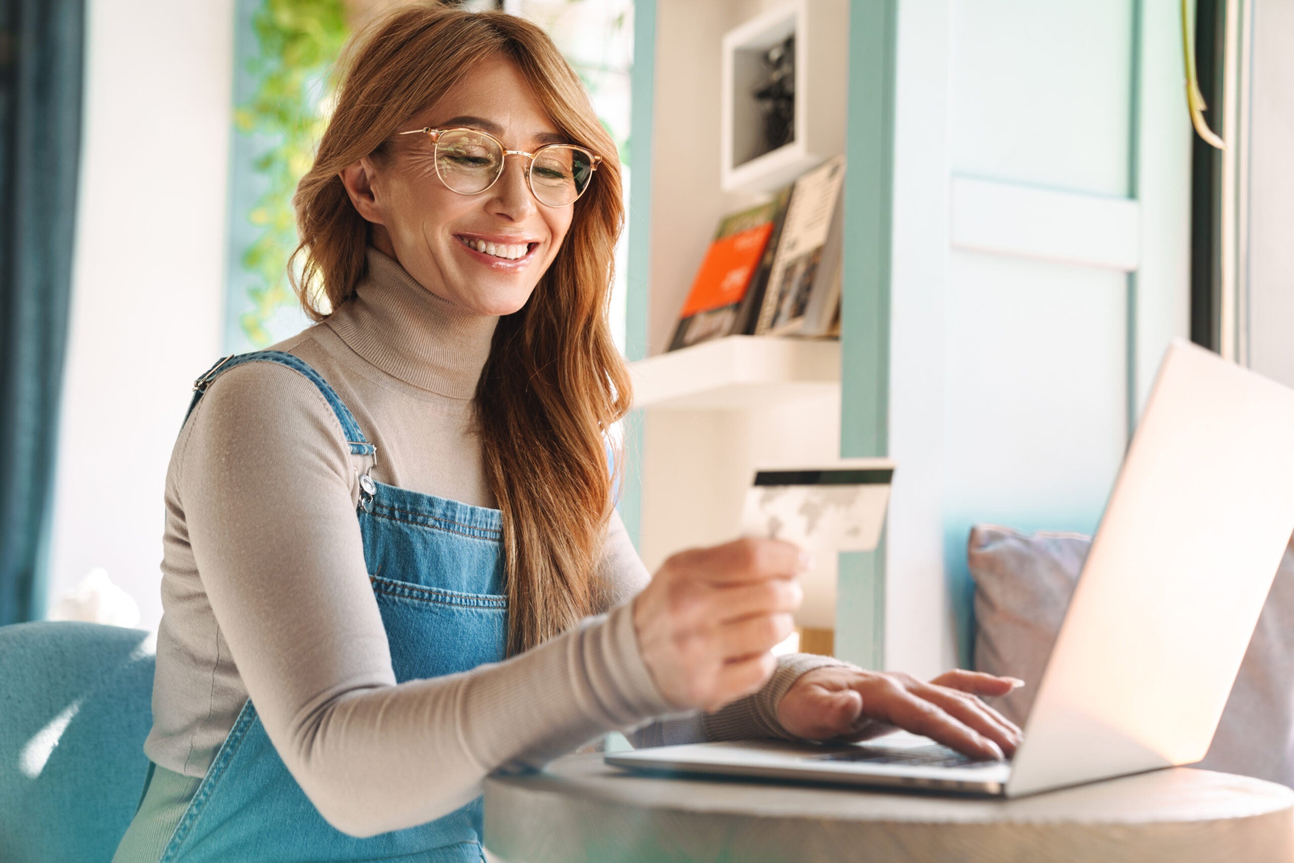 Photo of smiling woman holding credit card while using on laptop