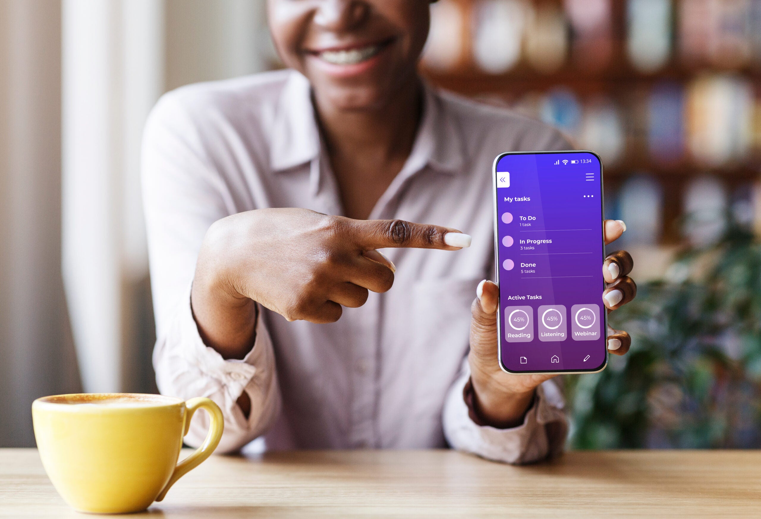 Unrecognizable black woman showing opened educational app on smartphone, pointing on screen, recommending modern application for onlin learning and distance study while sitting in cafe, collage