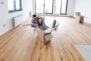 Young couple in new empty room of house. She is sitting on card box while he pushing her from behind