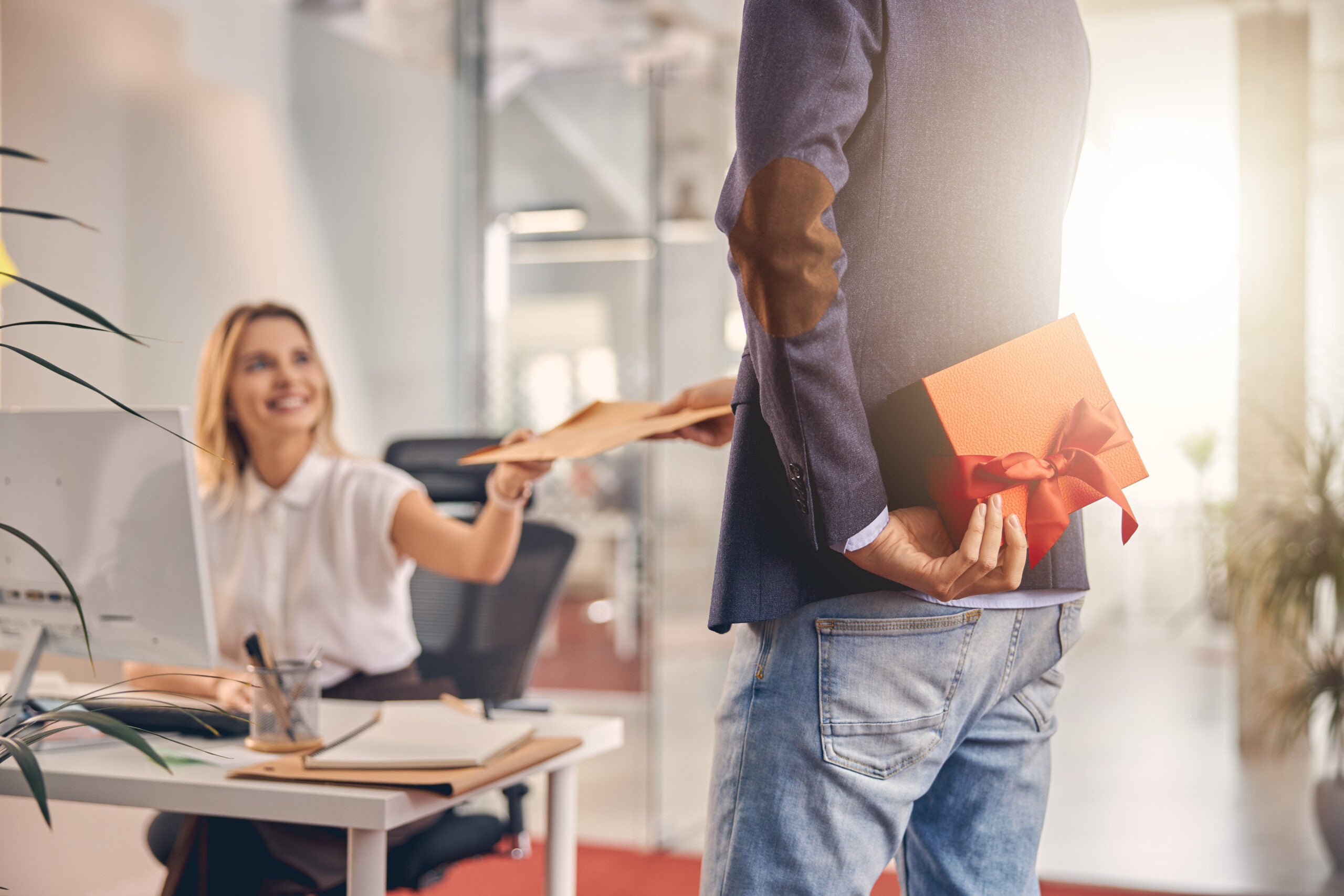 Close up smiling woman accepting papers from male colleague while gentleman holding gift box behind his back