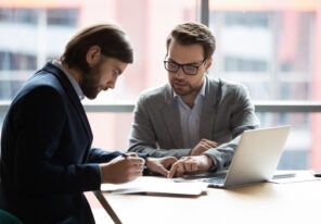 Focused young businessman signing agreement with skilled lawyer.