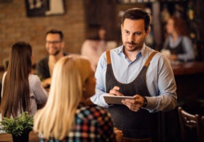 Waiter taking an order on touchpad while serving a guest in a bar.