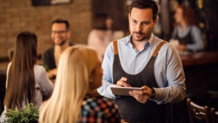 Waiter taking an order on touchpad while serving a guest in a bar.