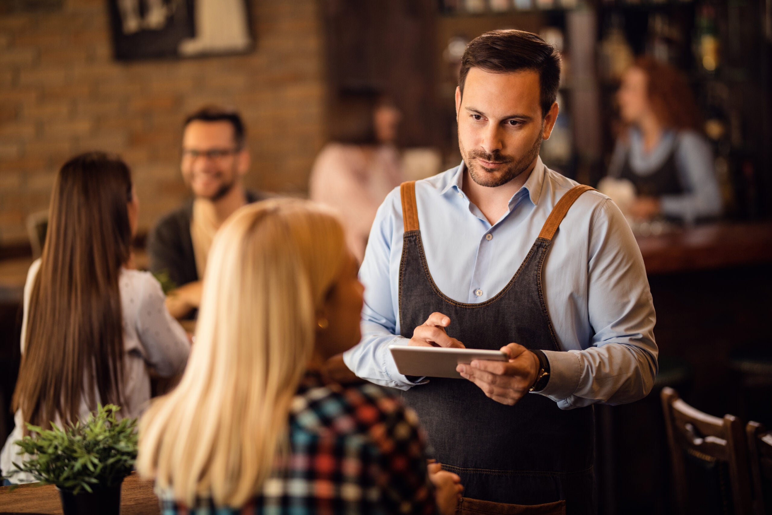 Waiter taking an order on touchpad while serving a guest in a bar.