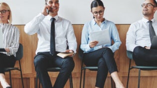 Group of diverse businesspeople smiling while sitting in a row in an office reception waiting for a meeting