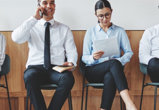 Group of diverse businesspeople smiling while sitting in a row in an office reception waiting for a meeting
