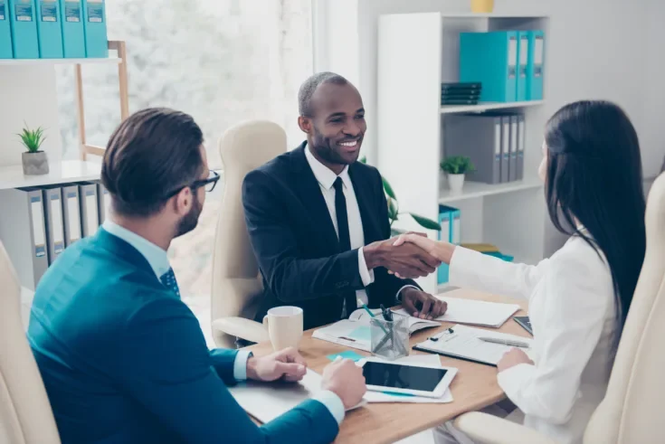 Partners making deal, shaking their hands, sitting in work place, wearing elegant, classic suits, to sign a contract, three professional, confident, stylish, attractive partners find a compromise