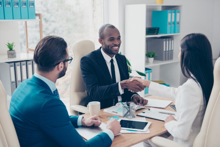 Partners making deal, shaking their hands, sitting in work place, wearing elegant, classic suits, to sign a contract, three professional, confident, stylish, attractive partners find a compromise