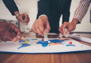 The hands of a group of businessmen holding chess and putting on a map.
