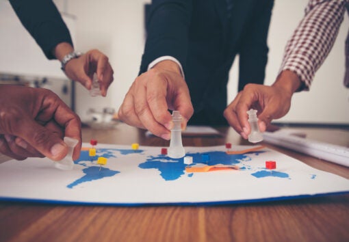 The hands of a group of businessmen holding chess and putting on a map.