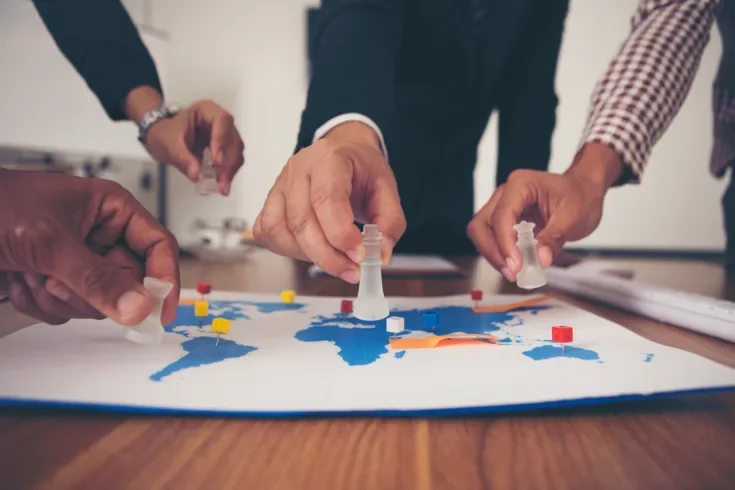 The hands of a group of businessmen holding chess and putting on a map.