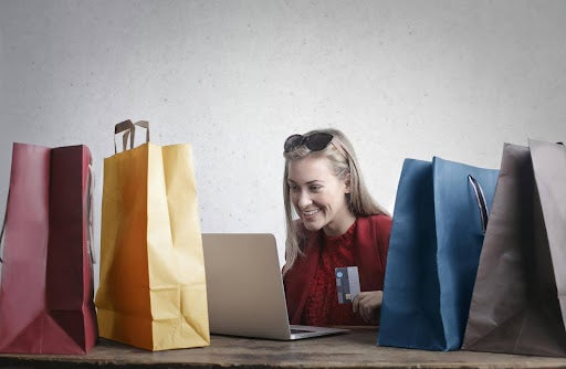 woman on laptop surrounded by shopping bags