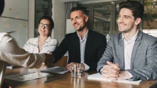 Three business partners in office handshaking with woman, as suc